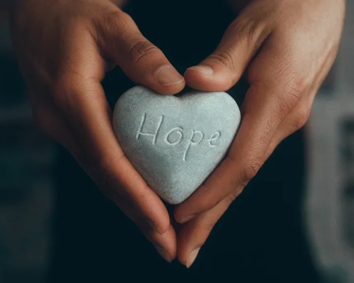 A person holding a stone in the shape of a heart that with Hope etched on it